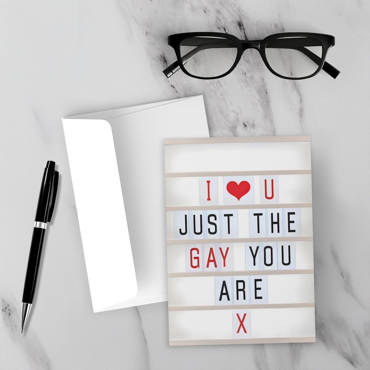 Light-up sign with 'I ❤️ U JUST THE GAY YOU ARE X' text on a marble surface with glasses and pen.
