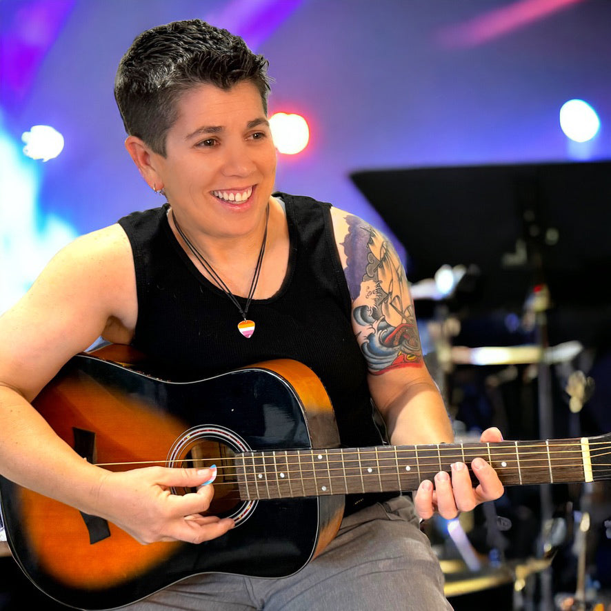 Person playing an acoustic guitar while wearing a lesbian pride guitar pick pendant necklace