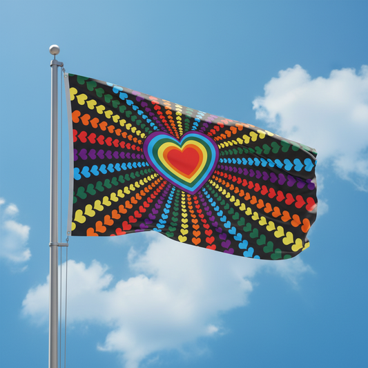 A black flag with a large rainbow heart in the center and radiating rows of small rainbow hearts on a blue sky with clouds background.