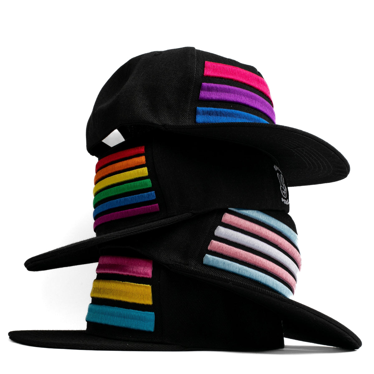 Four black hats stacked on top of each other.  Each with colorful embroidered pride striped bands on a white background