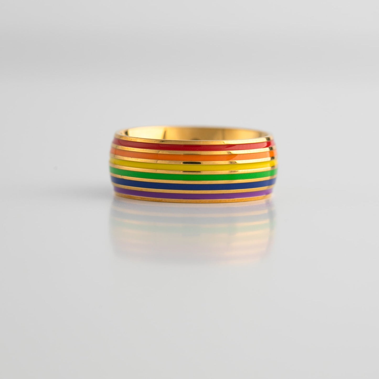 Gold ring with lgbtq pride rainbow band on a light gray background