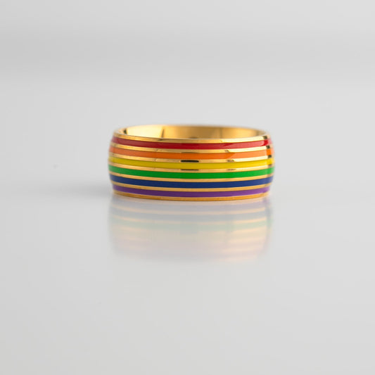 Gold ring with lgbtq pride rainbow band on a light gray background