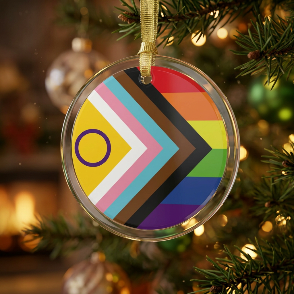 Round crystal clear glass holiday ornament with an intersex inclusive progress pride flag in the center hanging from a christmas tree with lights from a golden ribbon