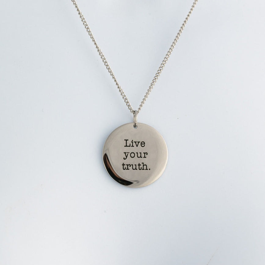 Silver necklace with a round pendant that says 'Live your truth' on a light gray background