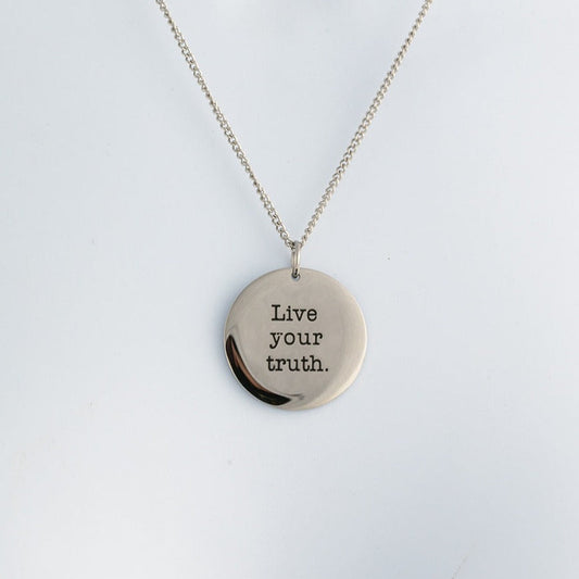 Silver necklace with a round pendant that says 'Live your truth' on a light gray background