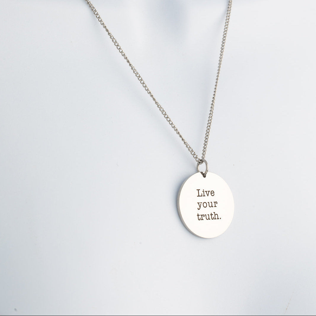 Silver necklace with a pendant that says 'Live your truth' on a light gray background