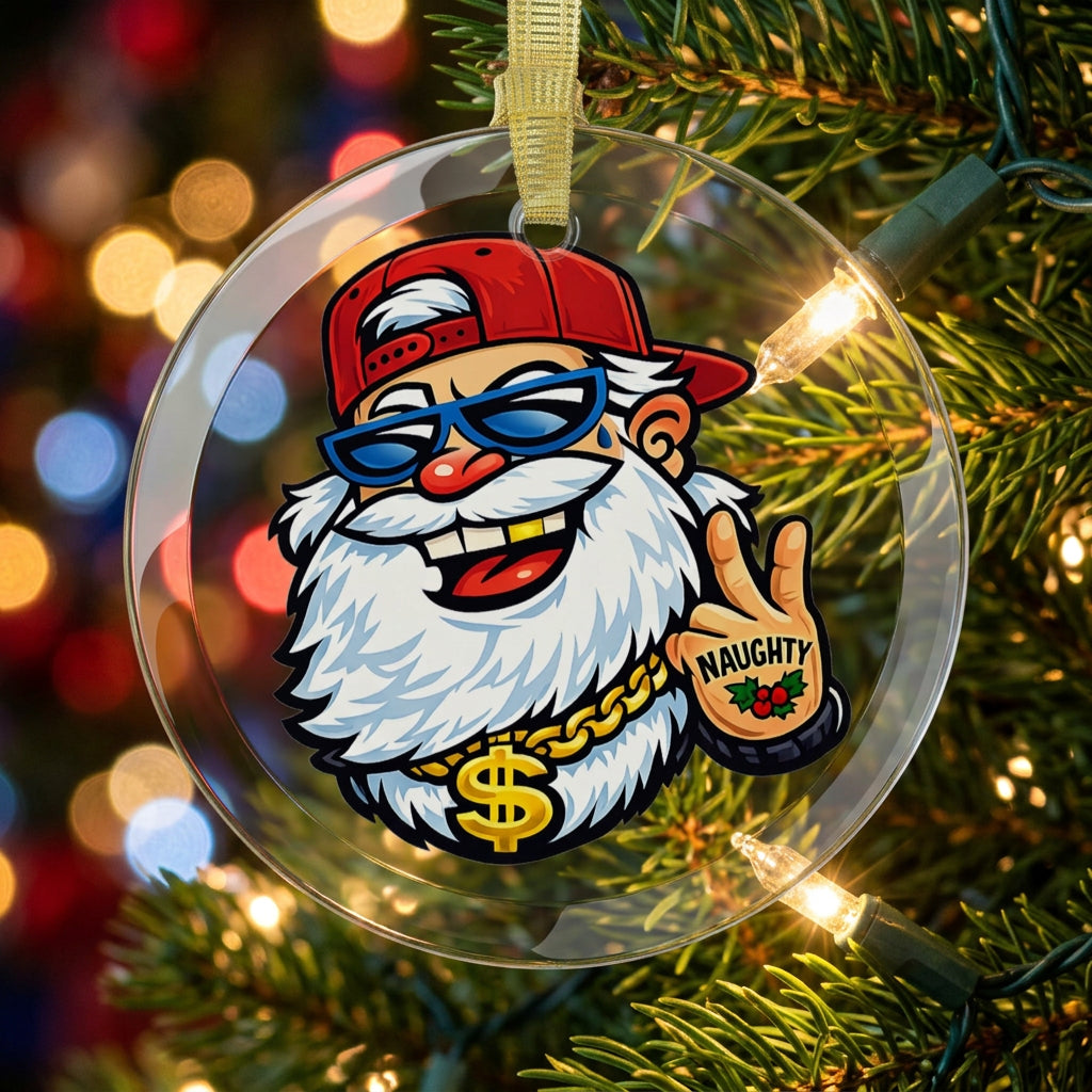 round clear glass holiday ornament hung from a christmas tree with lights.  The design is of Santa Claus face. Santa is wearing a backwards red baseball cap, sunglasses, a gold tooth, a gold chain around his neck, and making a peace sign with his left hand that has a tattoo on it that says 'Naughty' 