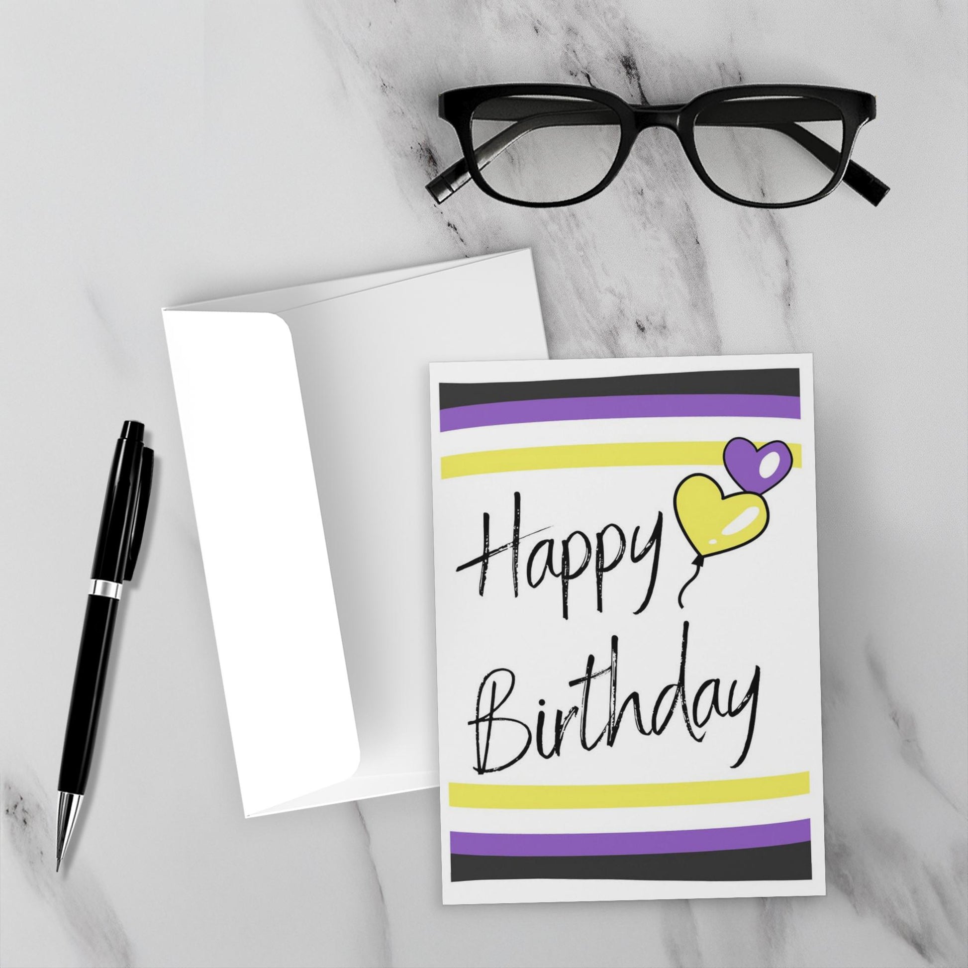 Nonbinary birthday card with heart and stripes on a marble surface with glasses and pen.