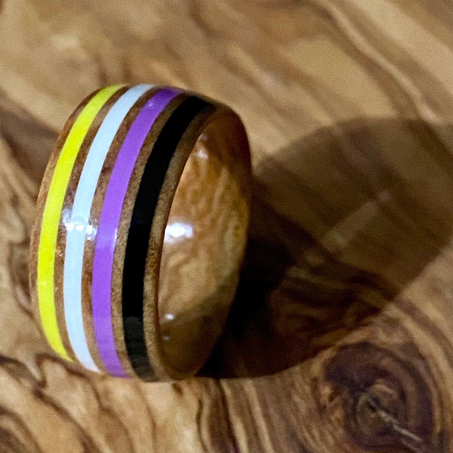 Wooden ring with nonbinary colored inlay on a wooden surface
