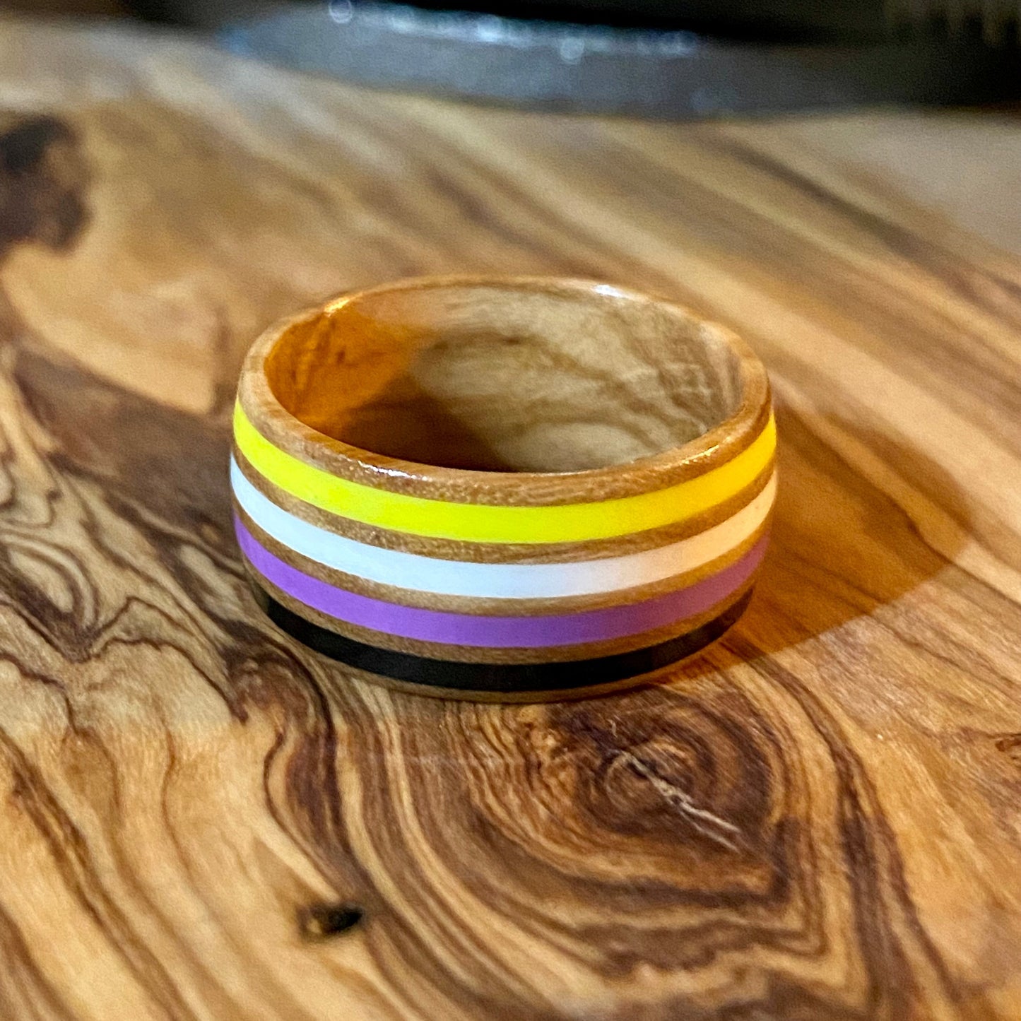 Wooden nonbinary pride ring with colorful stripes on a wooden surface