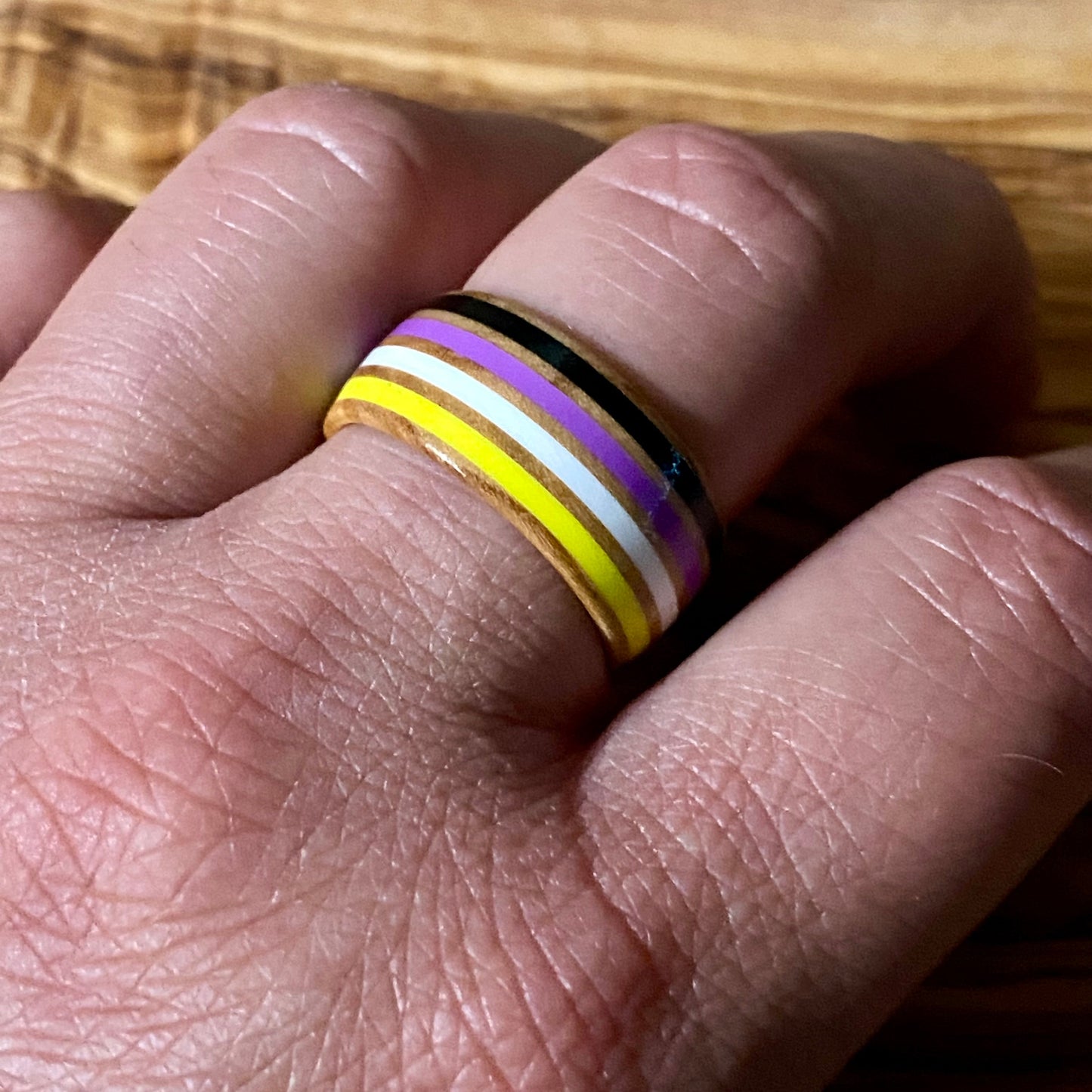 Close-up of a hand wearing a nonbinary striped ring on a wooden surface