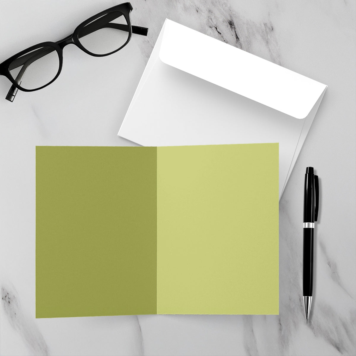 Inside of a christmas card with gold coloring and blank sentiment.  on a table with eyeglasses, pen, and envelope