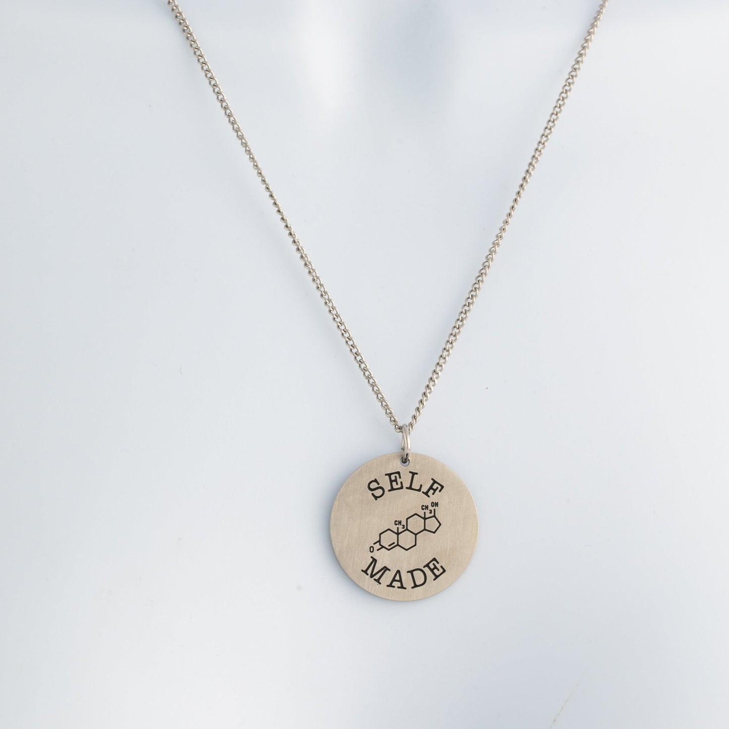 brushed steel necklace with a round pendant that says 'Self Made' on a white mannequin.