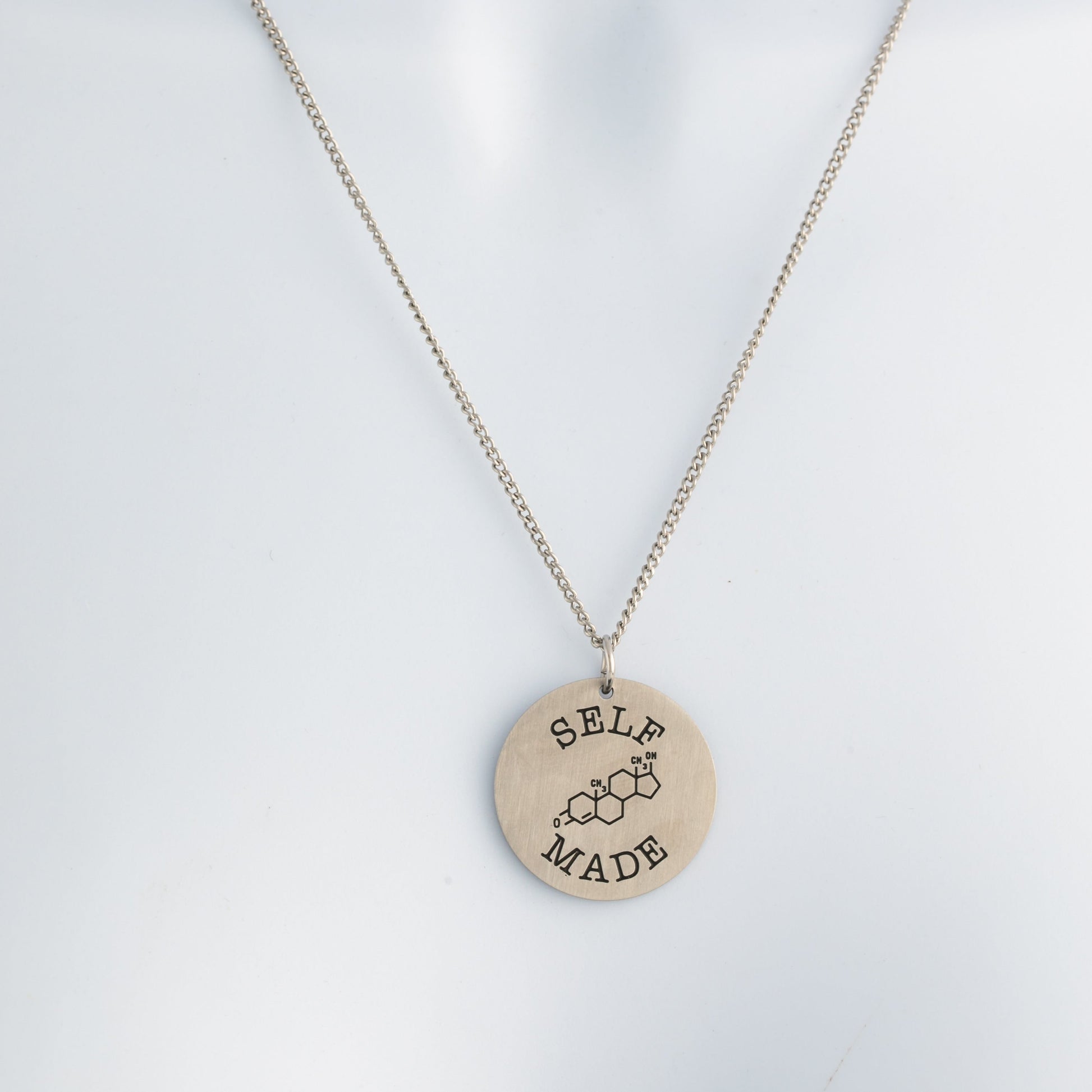 brushed steel necklace with a round pendant that says 'Self Made' on a white mannequin.