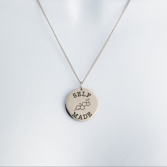Polished silver necklace with a round pendant with text that says 'self made' and the chemical symbol for testosterone on a light gray background