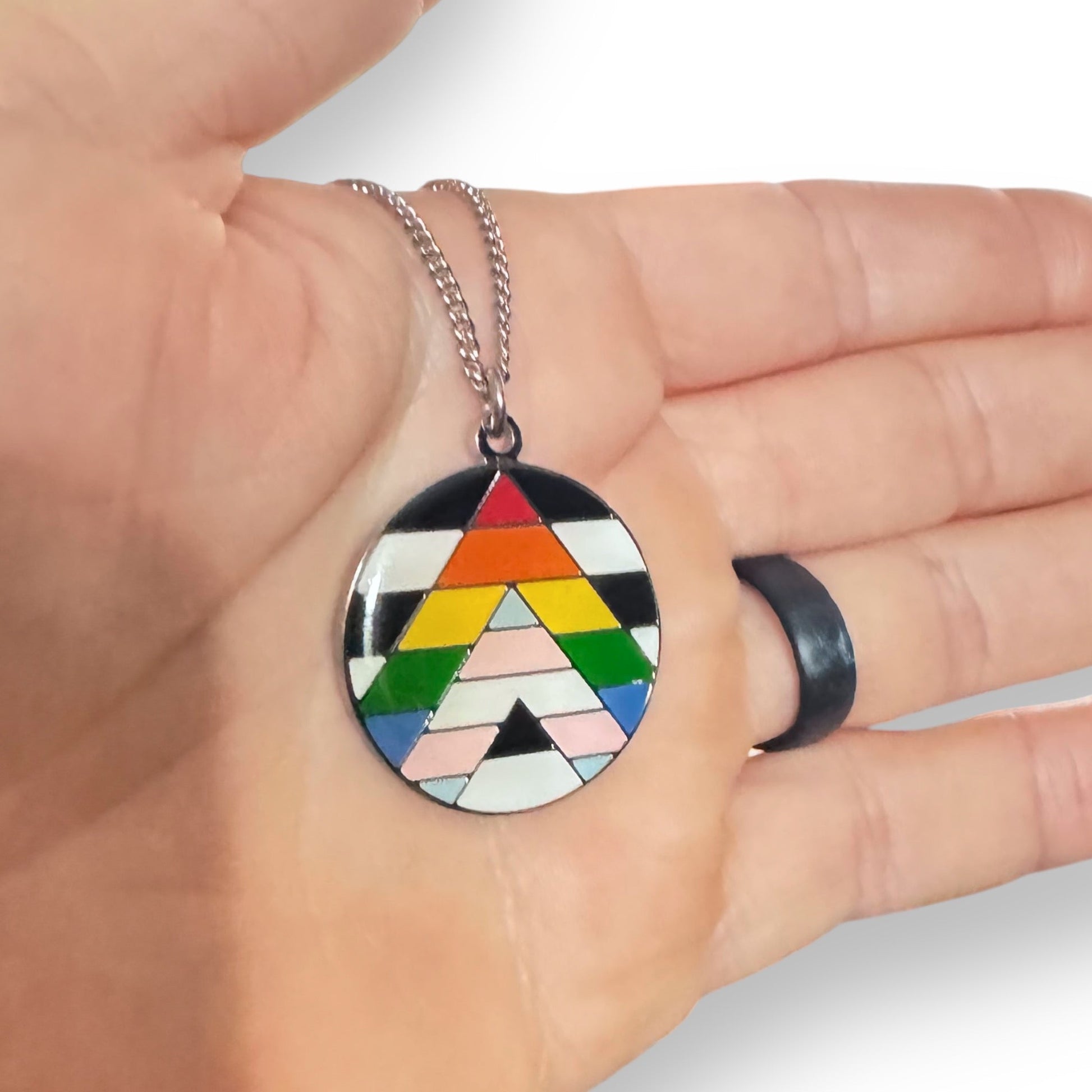 Colorful geometric pendant on a chain held in a hand against a neutral background