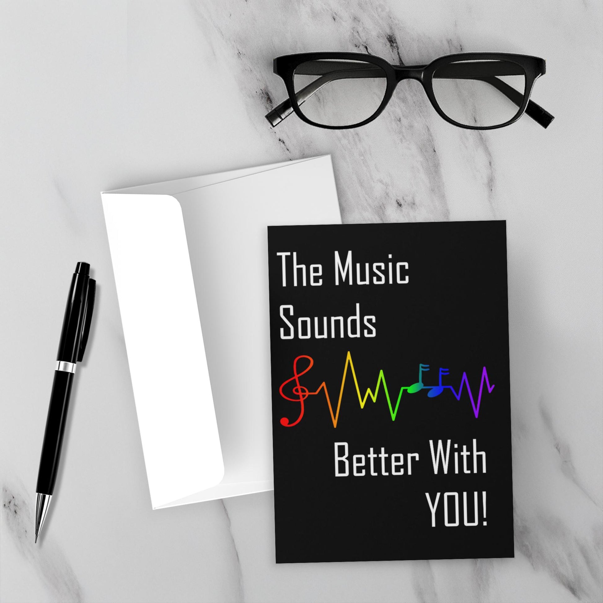 Greeting card with lgbtq rainbow musical notes and text on a marble surface with glasses and pen.