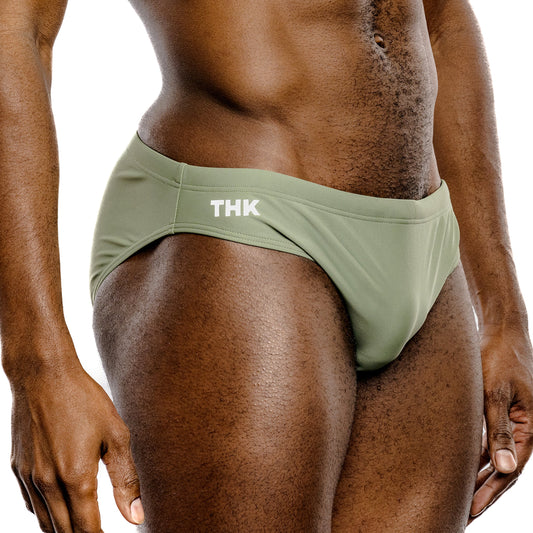 Person wearing green swim briefs with 'THK' branding on a white background