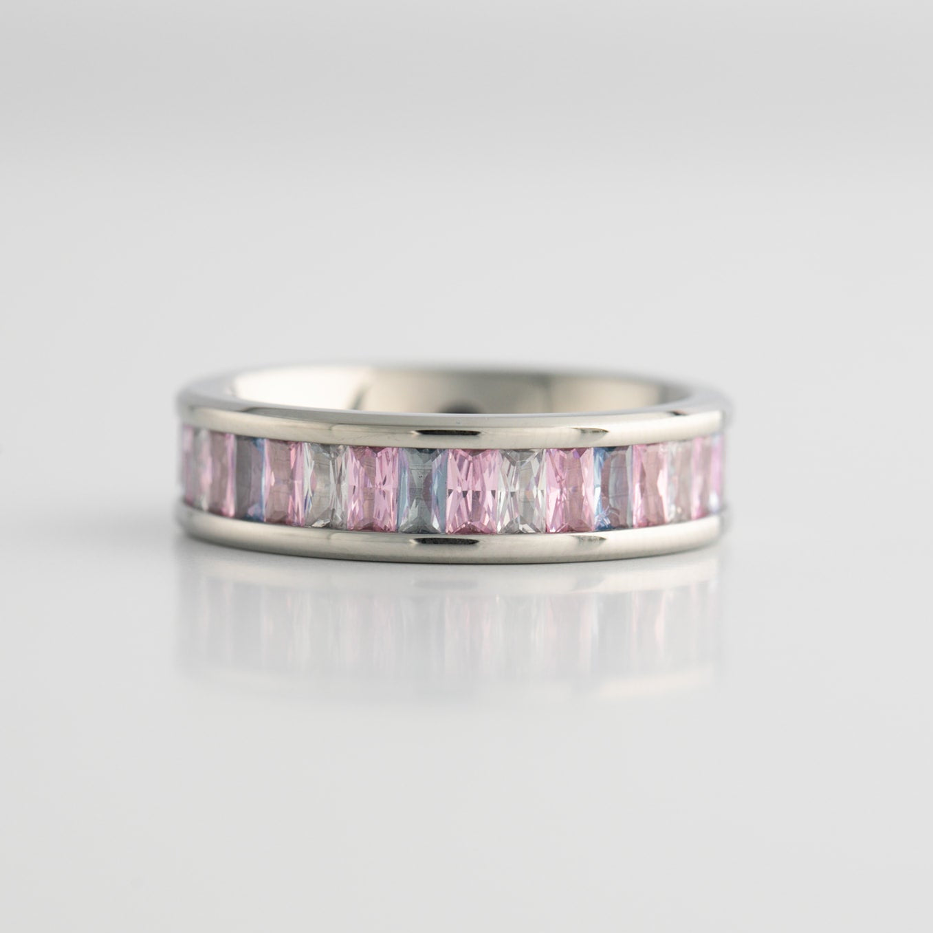 Silver ring with transgender pride colored gemstones on a light gray background