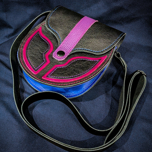 A black textured leather sporran with a bright pink, purple and blue bi pride design on the front flap, resting on a dark navy blue fabric background