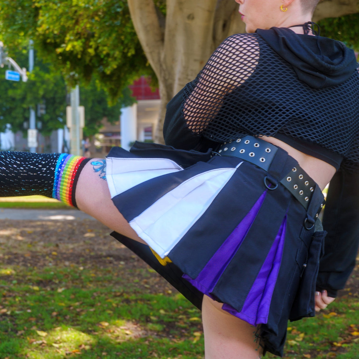Person wearing a black kilt with enby pride color accents in an outdoor setting