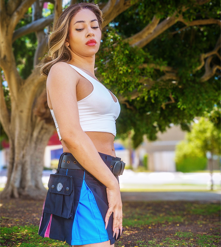 A person standing outdoors under a large tree, wearing a white sports top and a black kilt with bright blue and pink side panels, plus a utility belt pouch.