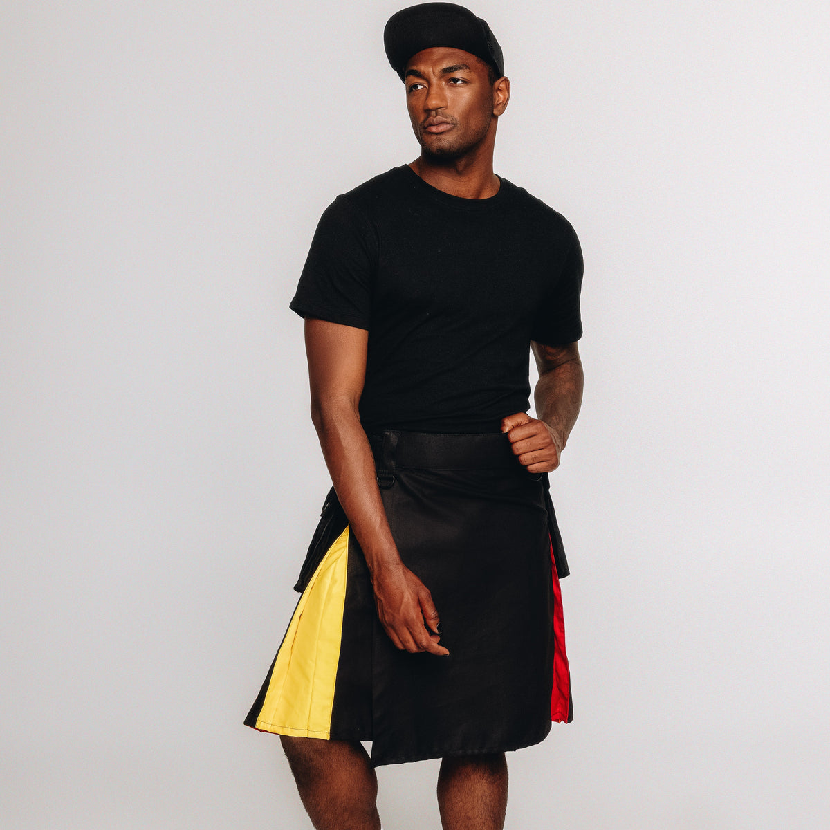 Person wearing a black t-shirt, black kilt with rainbow accents on a white background