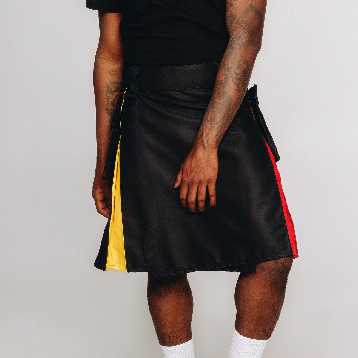 Person wearing a black leather kilt with rainbow accents on a white background