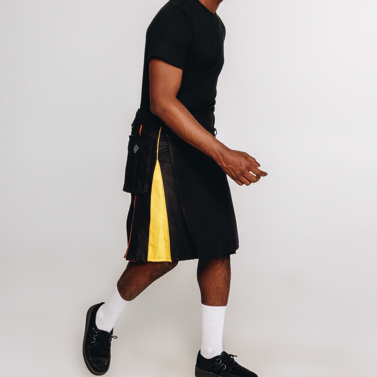 Man wearing a black t-shirt, black kilt with rainbow accents, and black sneakers on a white background
