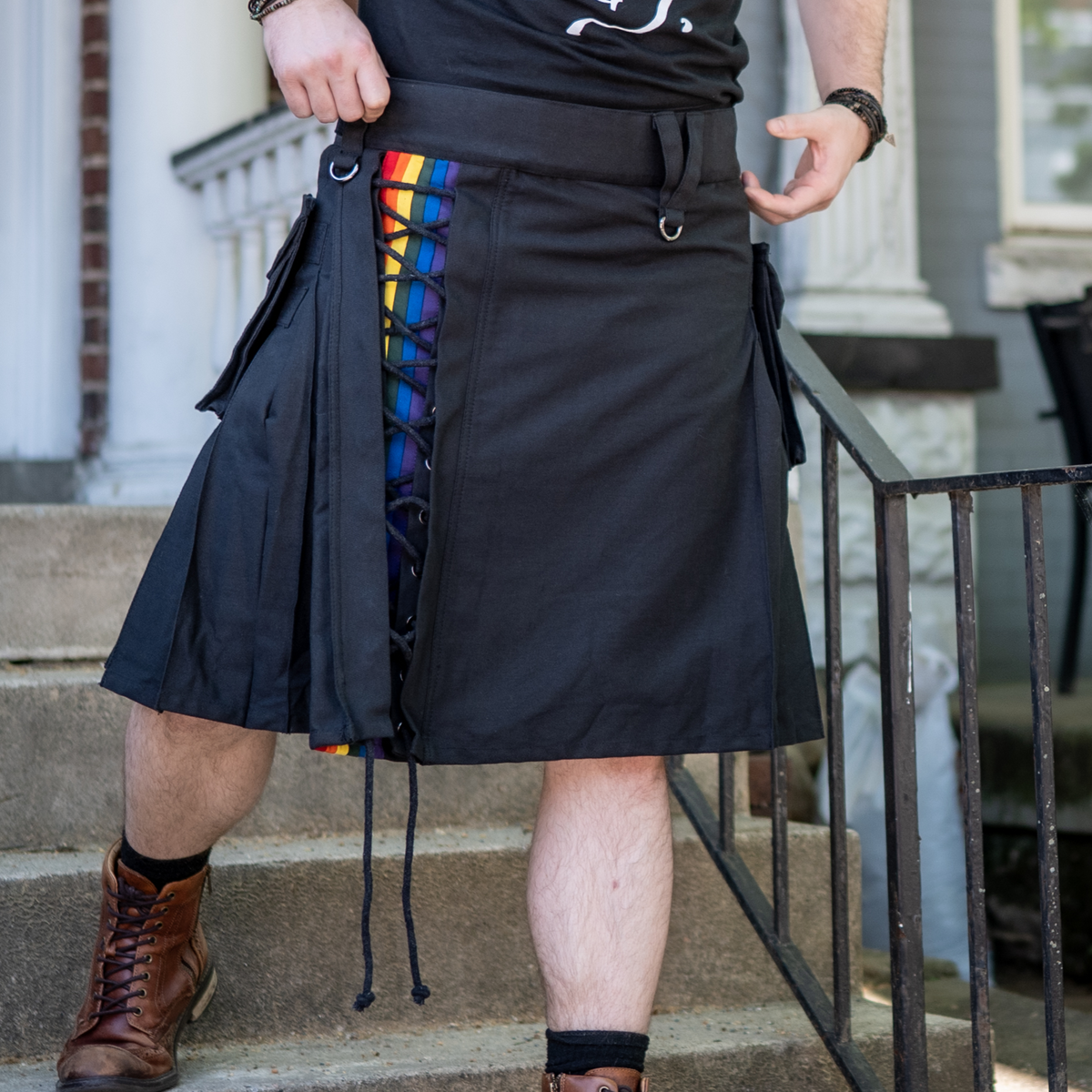 Person wearing a black kilt with rainbow accents on a staircase.